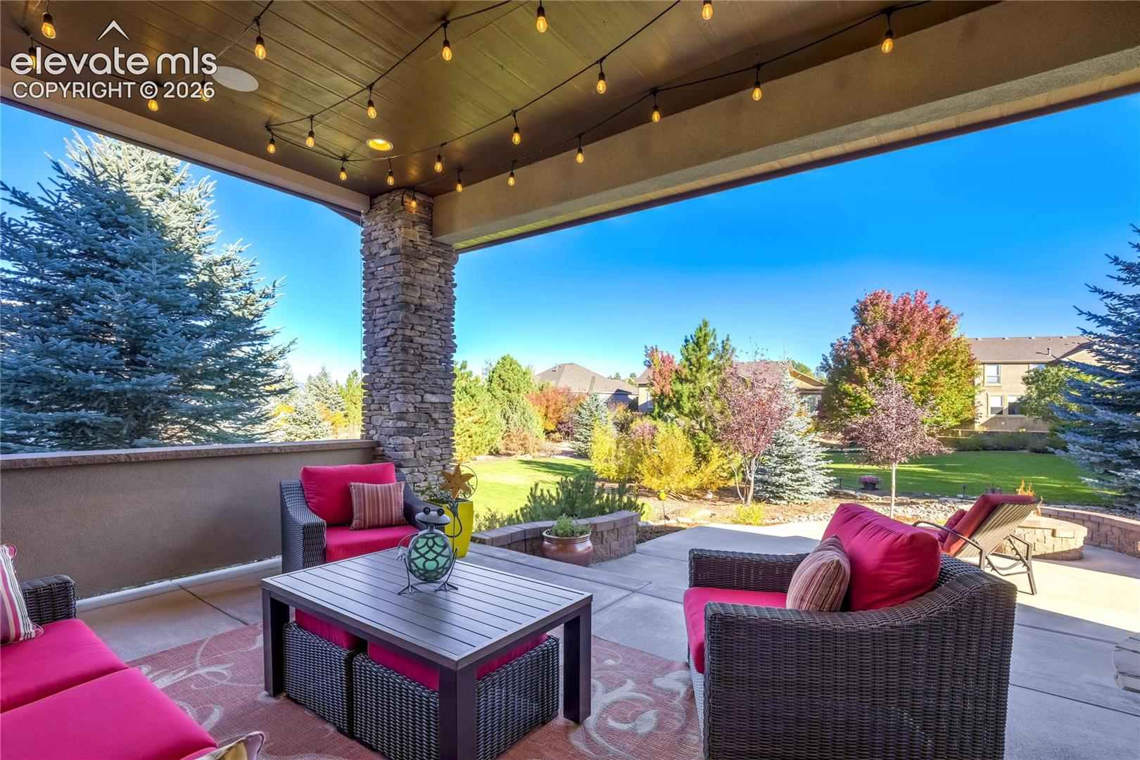 Relax beneath the beautifully finished covered patio, where substantial stone columns frame views of mature evergreens + colorful landscaping. A thoughtfully designed outdoor living space for morning coffee, conversation + peaceful evenings.
