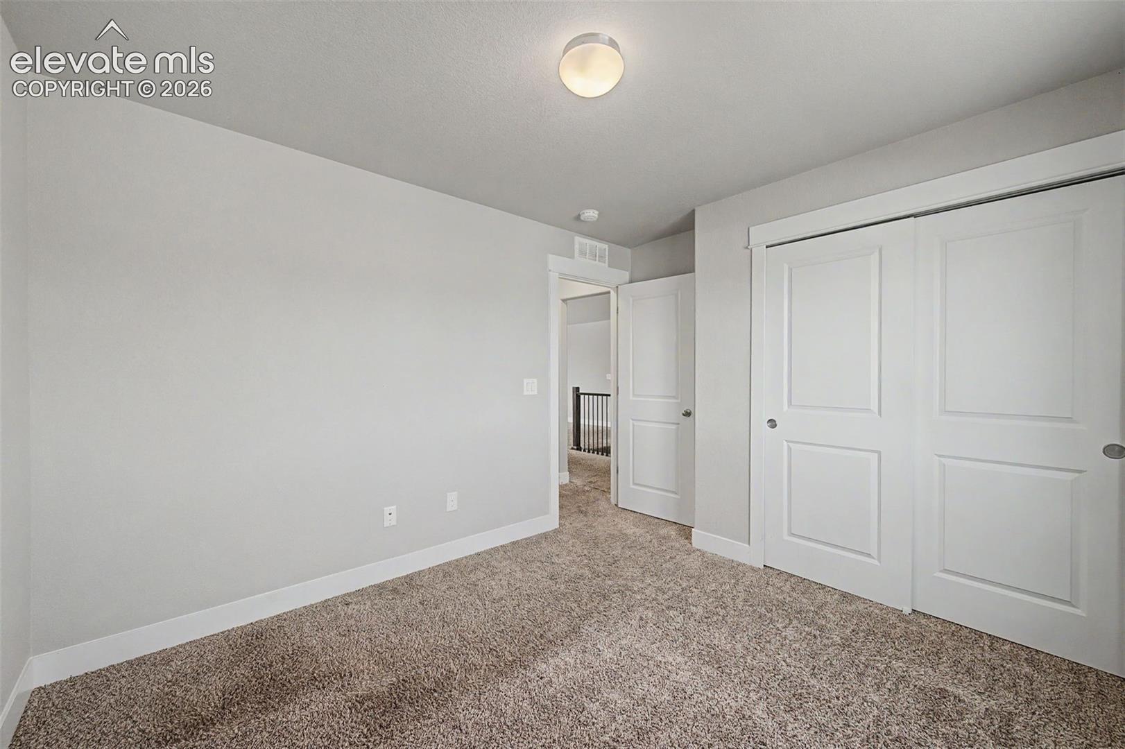 Bedroom featuring plush carpet flooring, a flush-mount ceiling light, white baseboards, and bi-fold closet doors