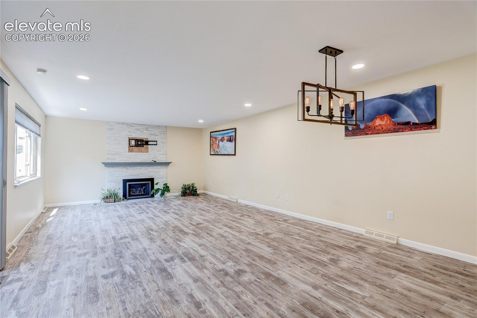 Living area featuring wood-finish flooring, a stone-surround fireplace with a mantel, recessed lighting, and a geometric multi-light chandelier