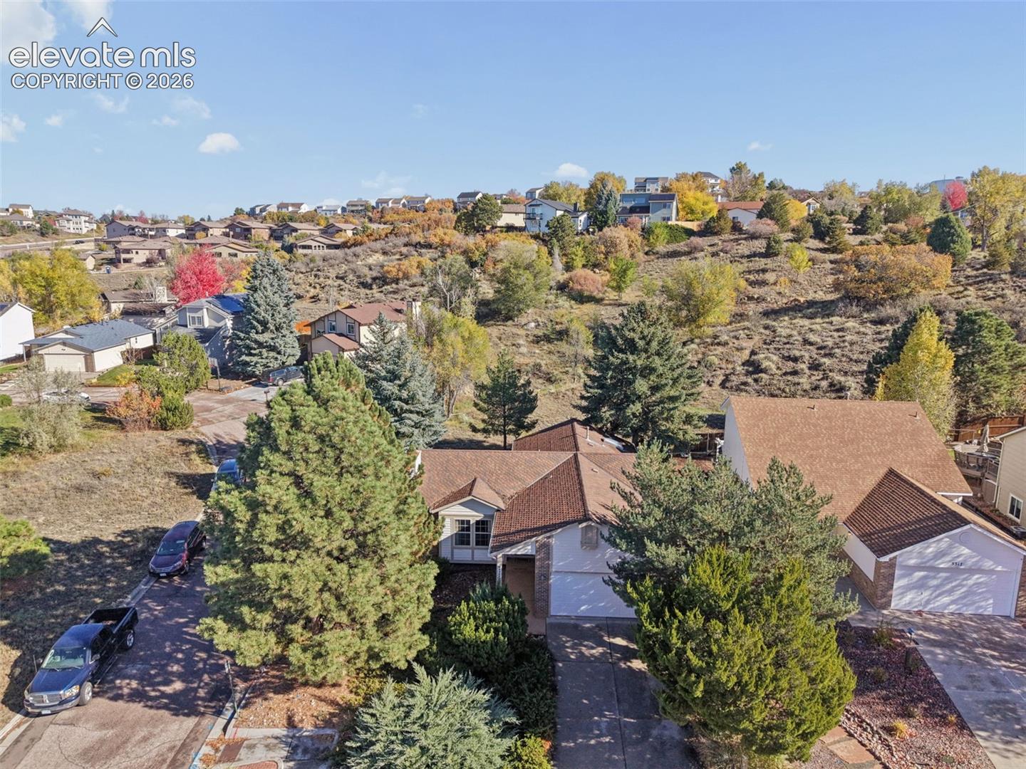 Aerial perspective of a multi-gabled residence featuring a concrete driveway, two-car garage, and established landscaping with mature coniferous trees