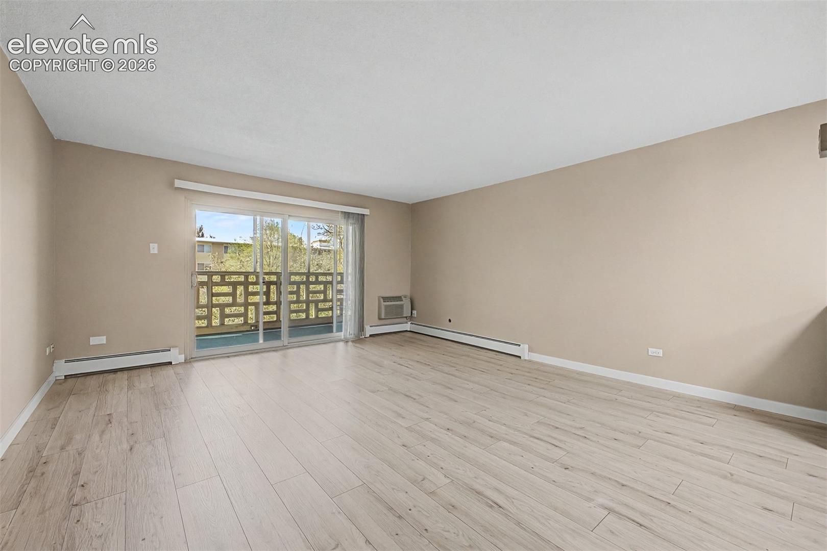 Spacious room featuring light wood-finish flooring, neutral wall tones, and baseboard heating