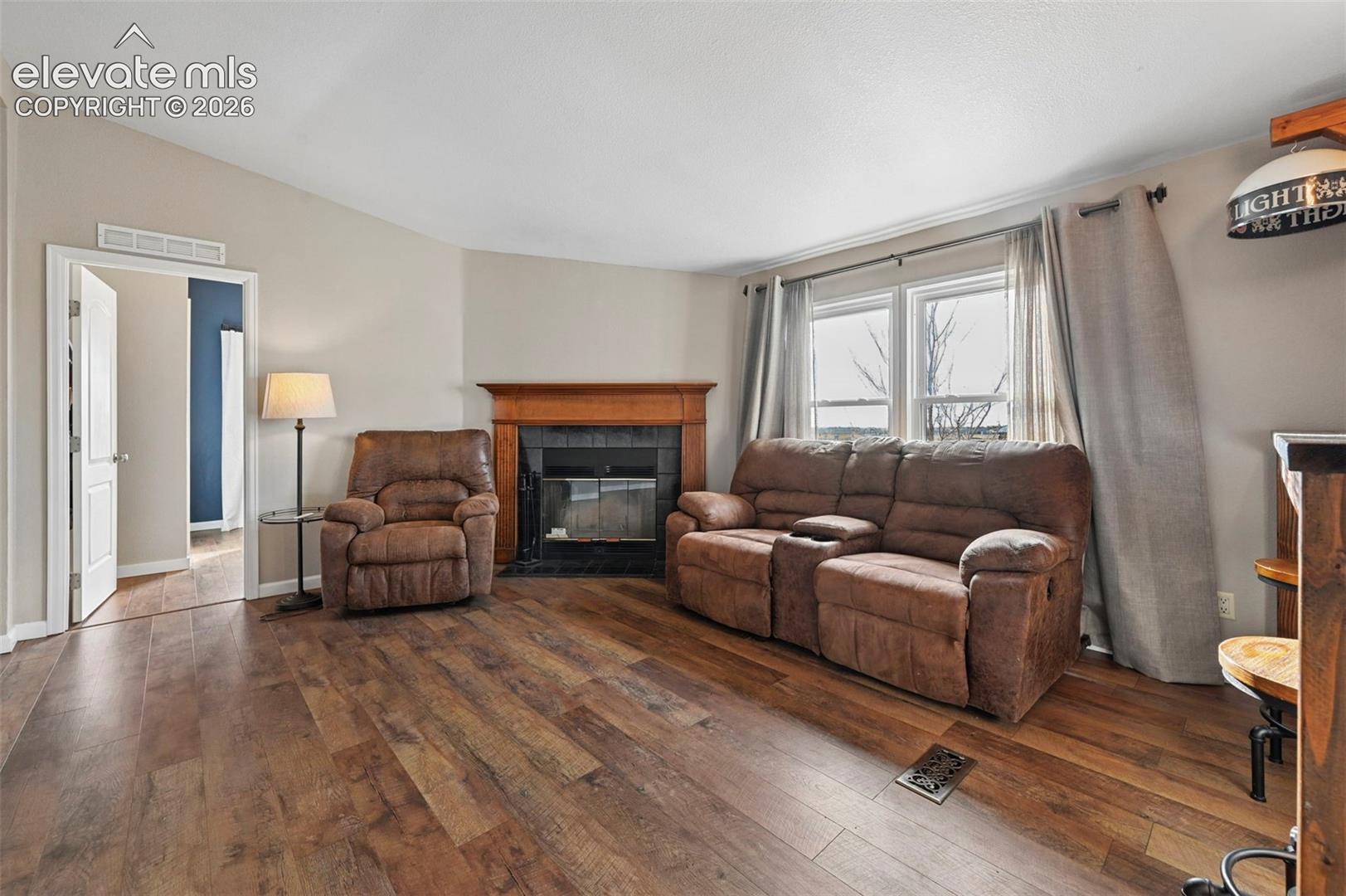 Living area featuring wood-finish flooring, a fireplace with a wood mantel and dark tile surround, and dual pane windows