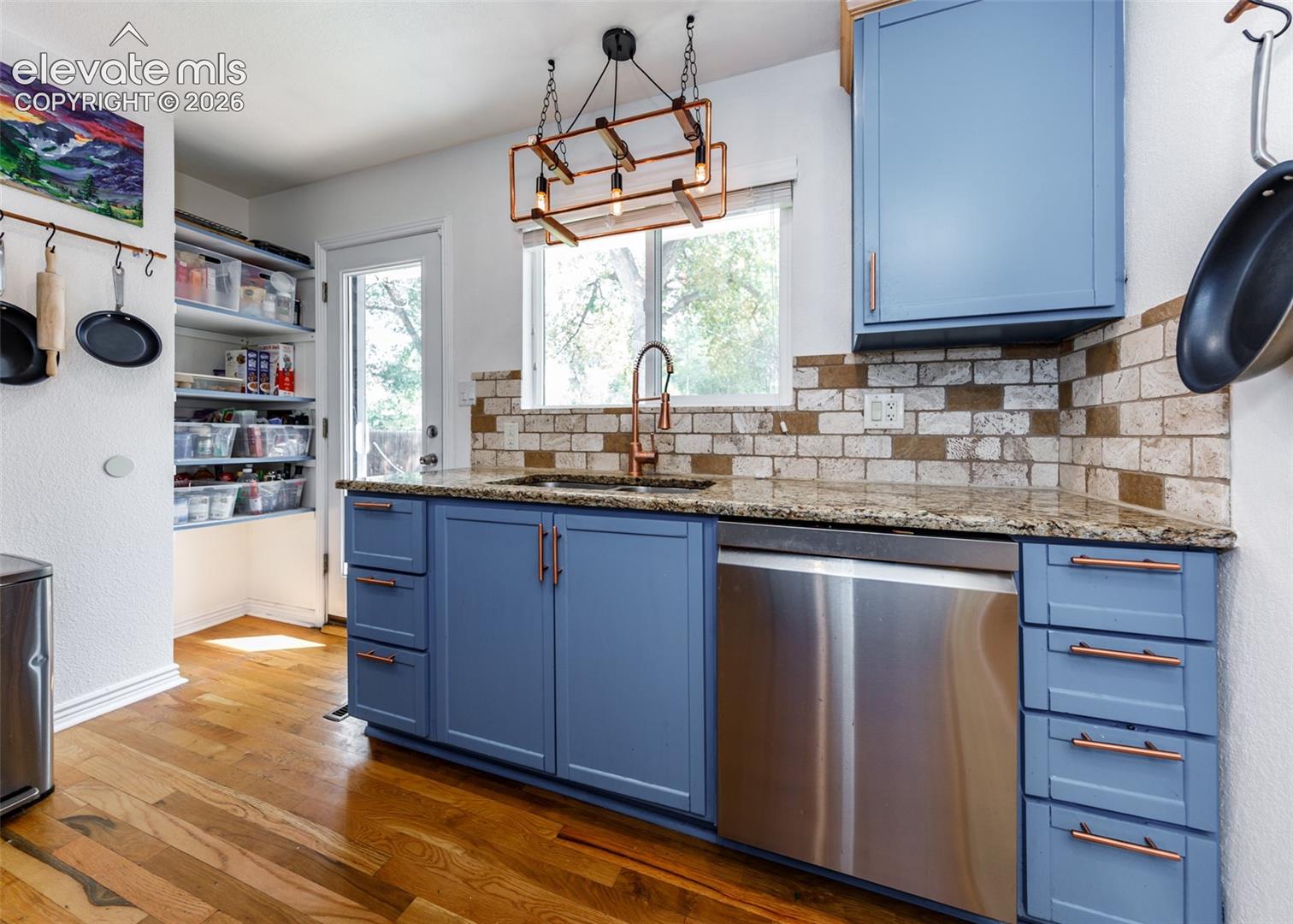 Kitchen featuring wood-finish flooring, blue cabinetry with copper-toned hardware, a stainless steel dishwasher, and a stone-finish countertop
