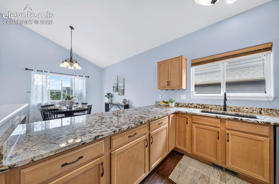 Kitchen featuring stone-surface countertops, wood-finish cabinetry, a drop-in sink with a matte black faucet, vaulted ceilings, and an overhead pendant light fixture