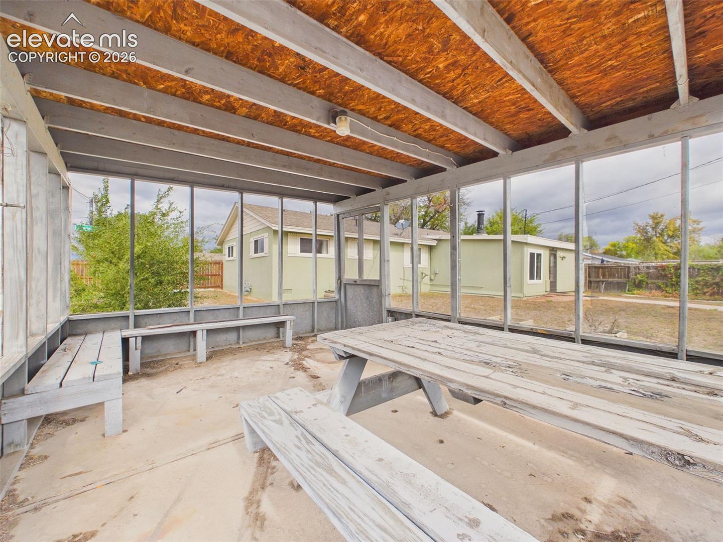 Detached screened enclosure featuring built-in bench seating, a picnic table, and views of the backyard. A flexible outdoor gathering space with potential for relaxing and entertaining.