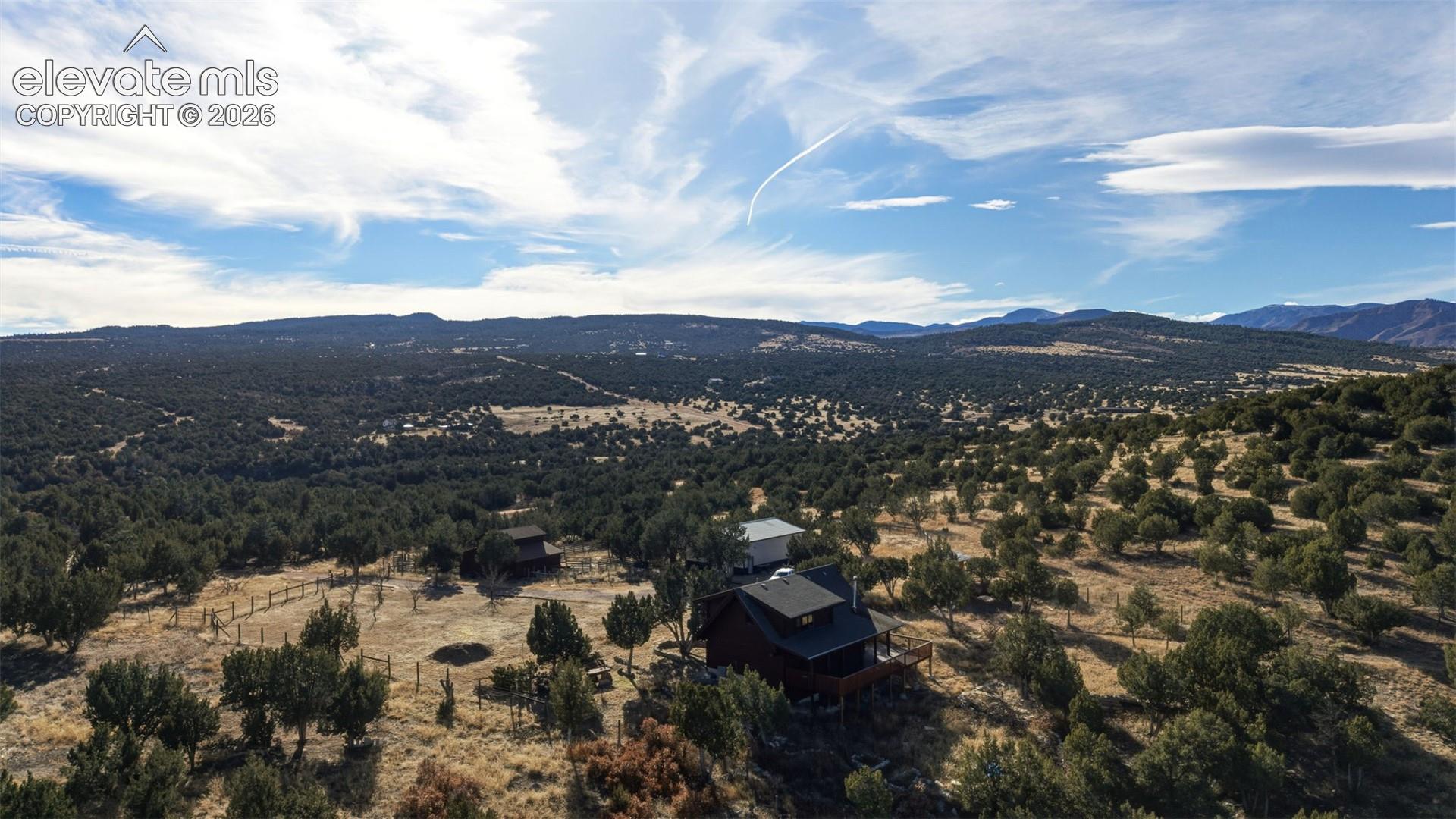 Expansive natural landscape with scattered trees, mountainous backdrop, and a single-story dwelling with a dark roof