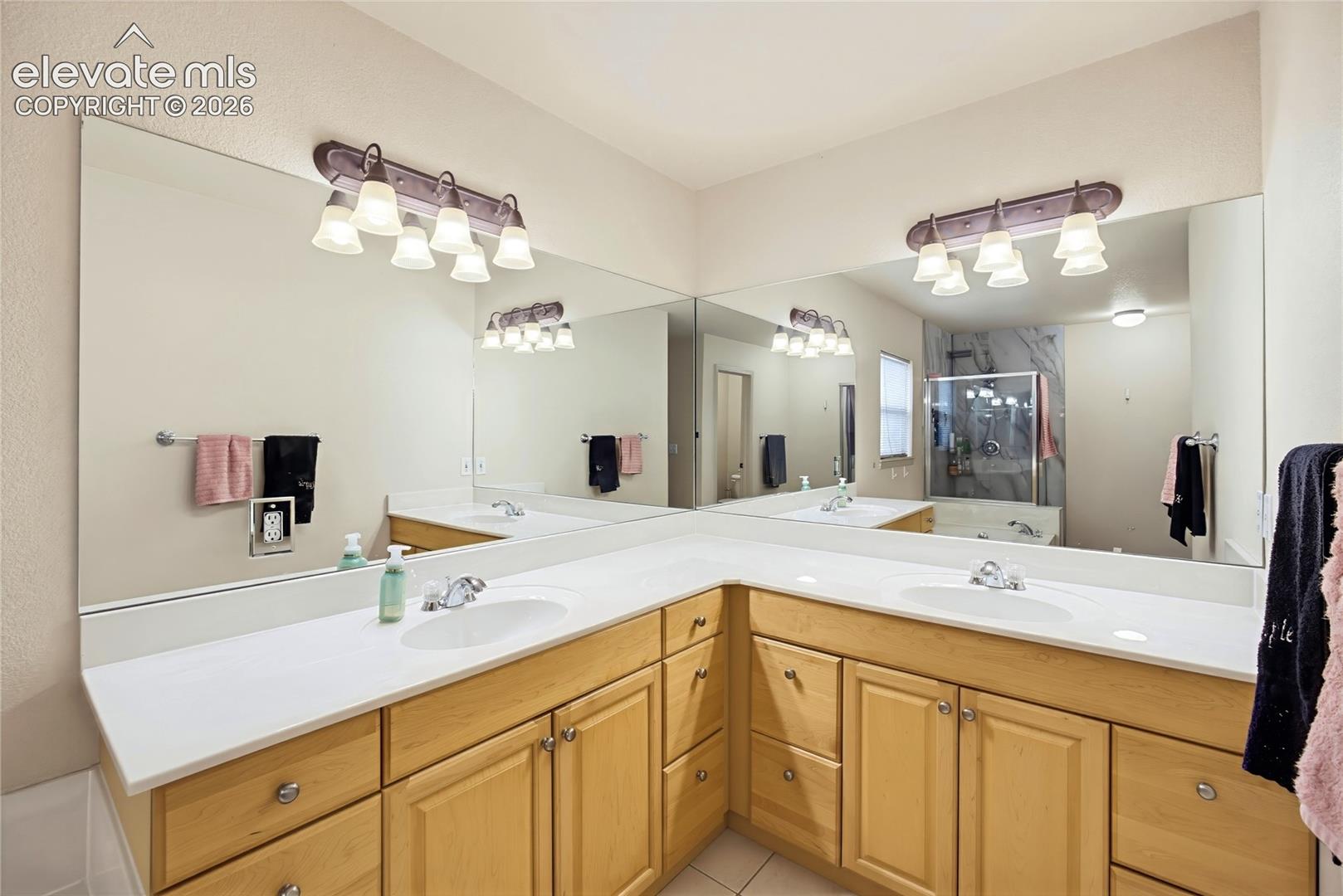 Dual vanity with light wood cabinetry, white countertops, and integrated sinks