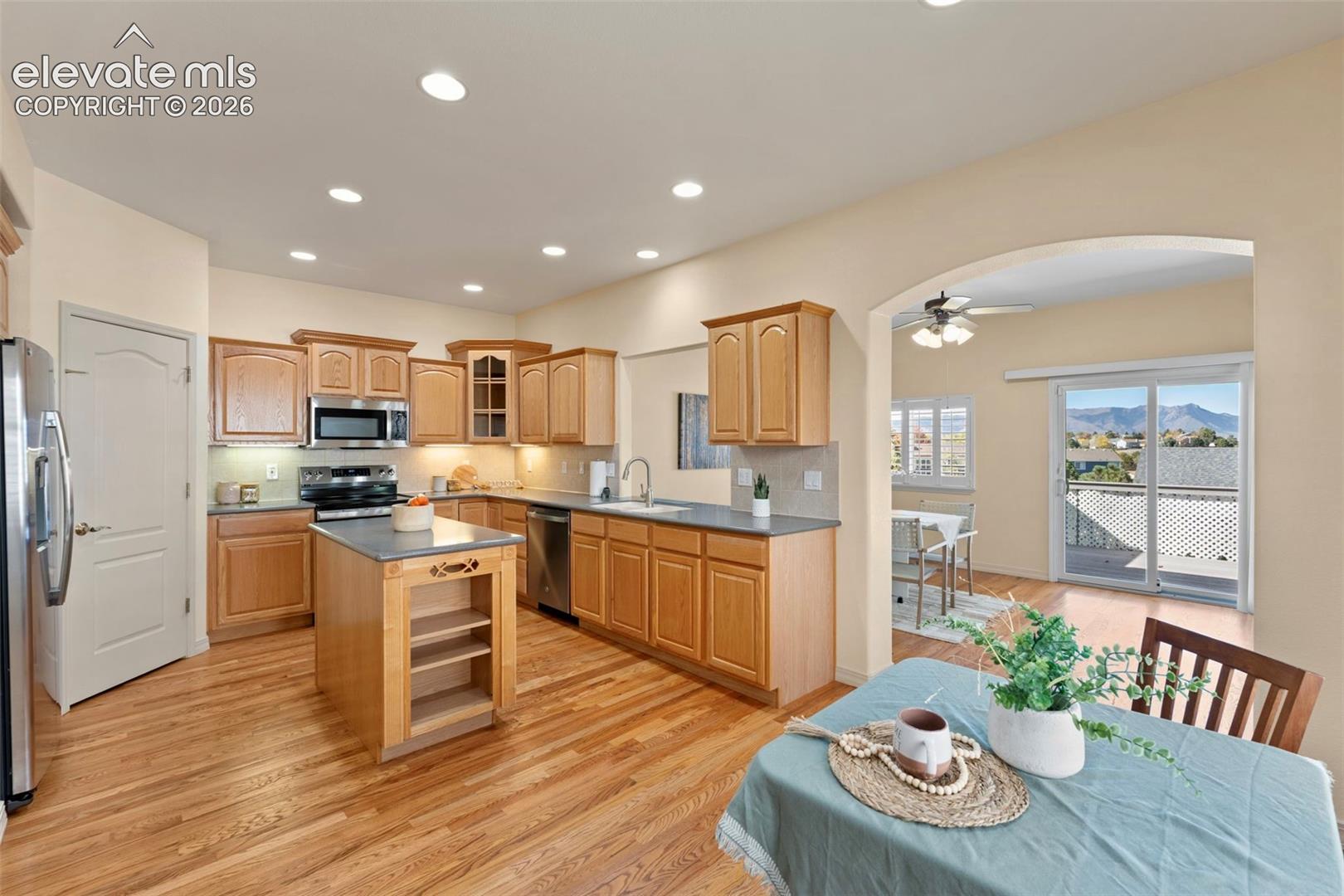 Kitchen featuring wood cabinetry, a center island with open shelving, integrated stainless steel appliances, dark stone countertops, and wood-finish flooring