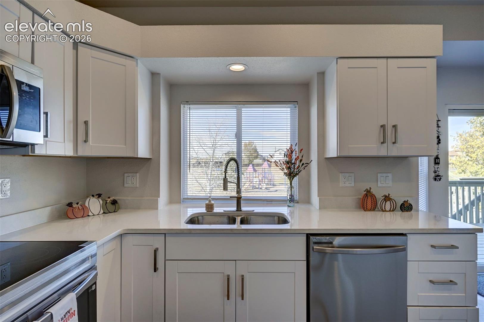 Kitchen featuring white shaker-style cabinetry, a solid-surface countertop, an undermount double-basin stainless steel sink, a pull-down gooseneck faucet, and stainless steel appliances