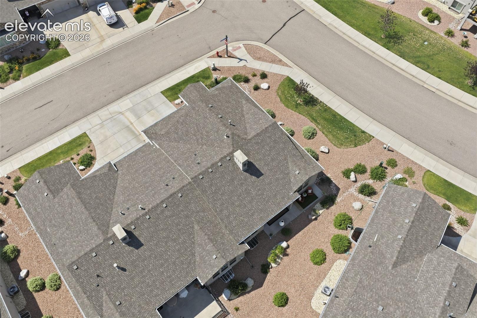 Gray shingle roofing, paved driveway, landscaped yard with crushed rock and mature shrubs, paved sidewalk, and street frontage.