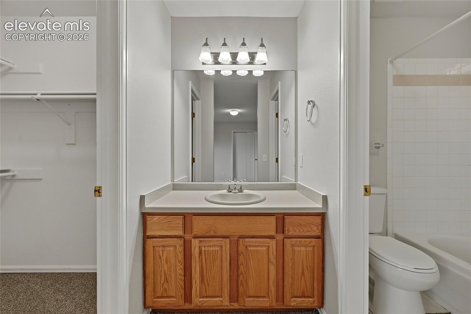 Bathroom featuring a vanity with wood cabinetry, a solid-surface countertop, an inset basin, a framed mirror, and a four-bulb light fixture