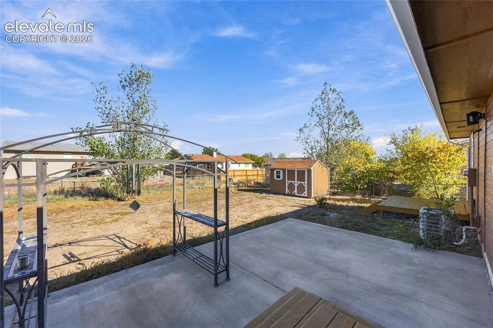 Rear concrete patio featuring a detached storage shed, exterior wood siding, and an open backyard area