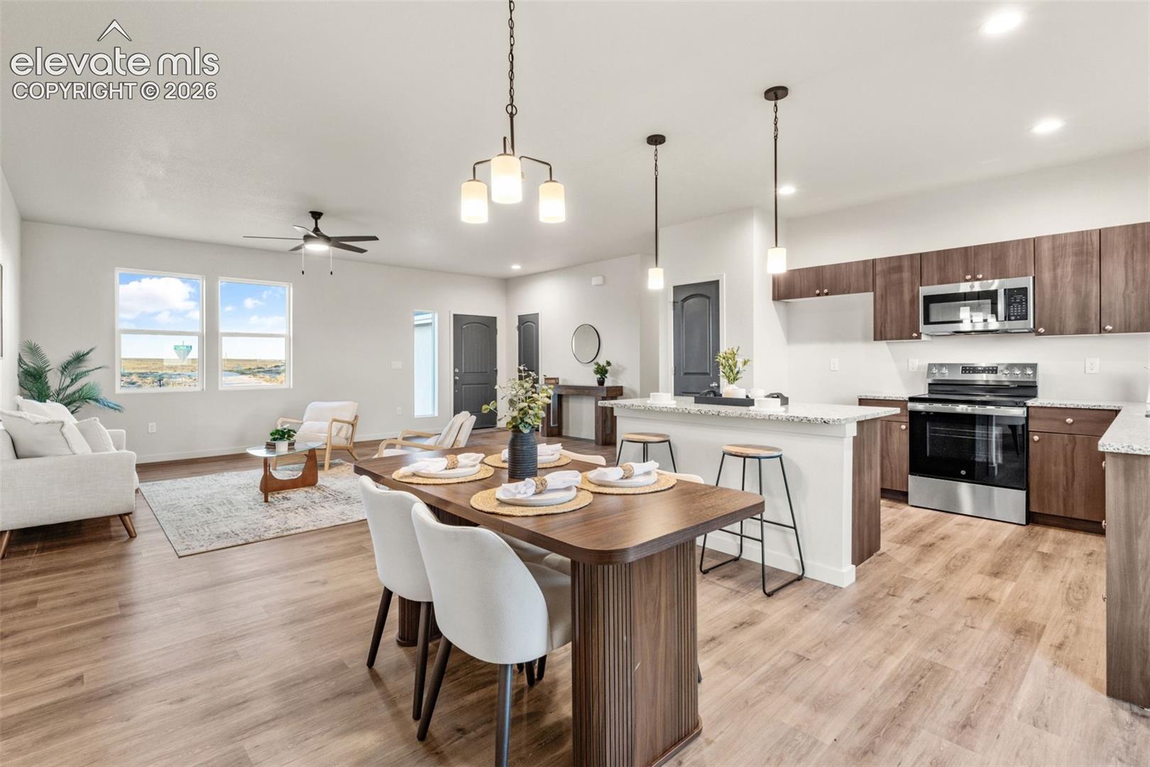 Open-concept area featuring wood-finish flooring, a kitchen island with stone-composite countertops, stainless steel appliances, and pendant lighting