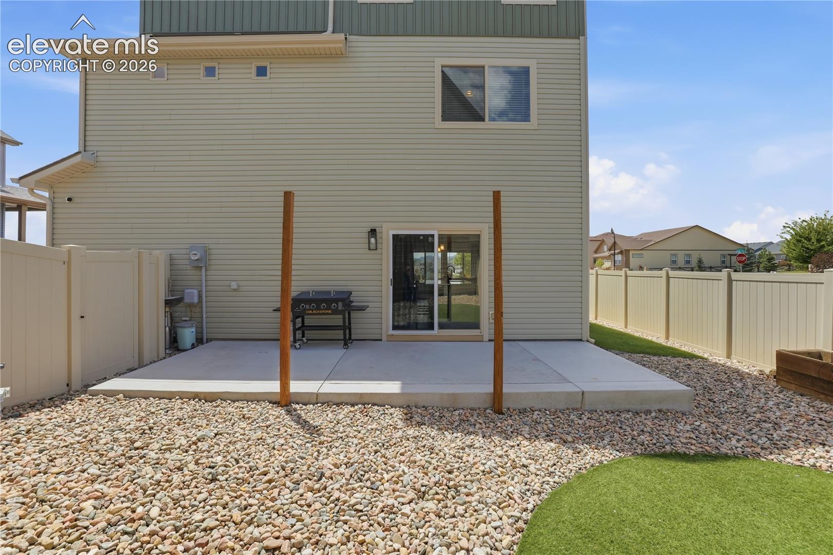 Exterior patio featuring poured concrete, privacy fencing, gravel landscaping, and artificial turf