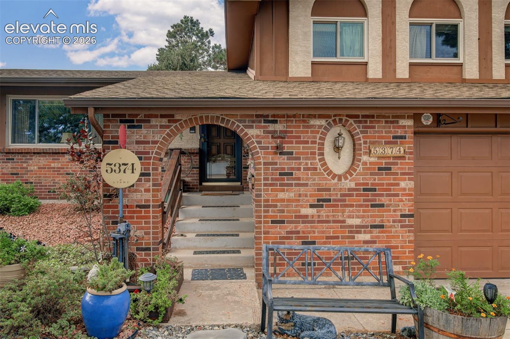 Brick exterior with an arched entry, concrete steps, and an integrated garage