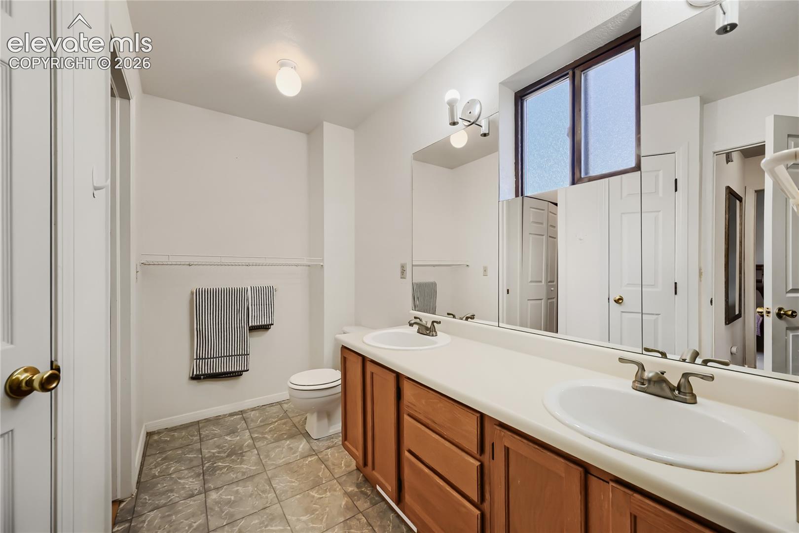 Double vanity with integrated sinks, wood-finish cabinetry, a large mirrored wall, and tiled flooring