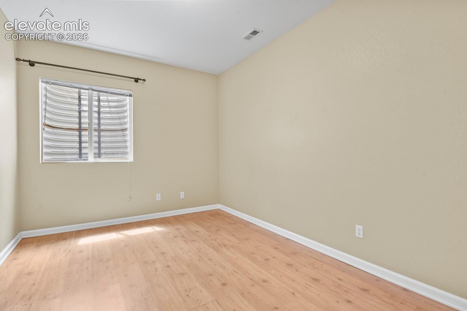 Room featuring wood-finish flooring, a neutral wall palette, white baseboards, and a window