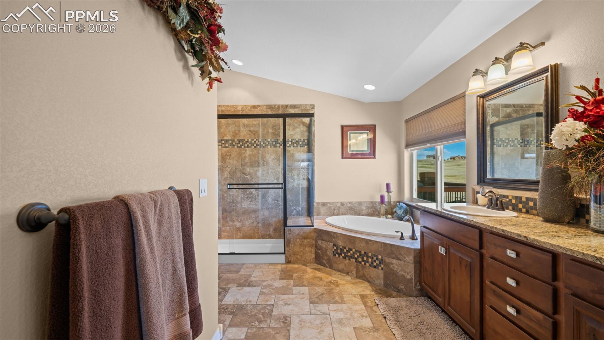 Bathroom with a shower stall, lofted ceiling, light stone finish floors, a bath, and vanity