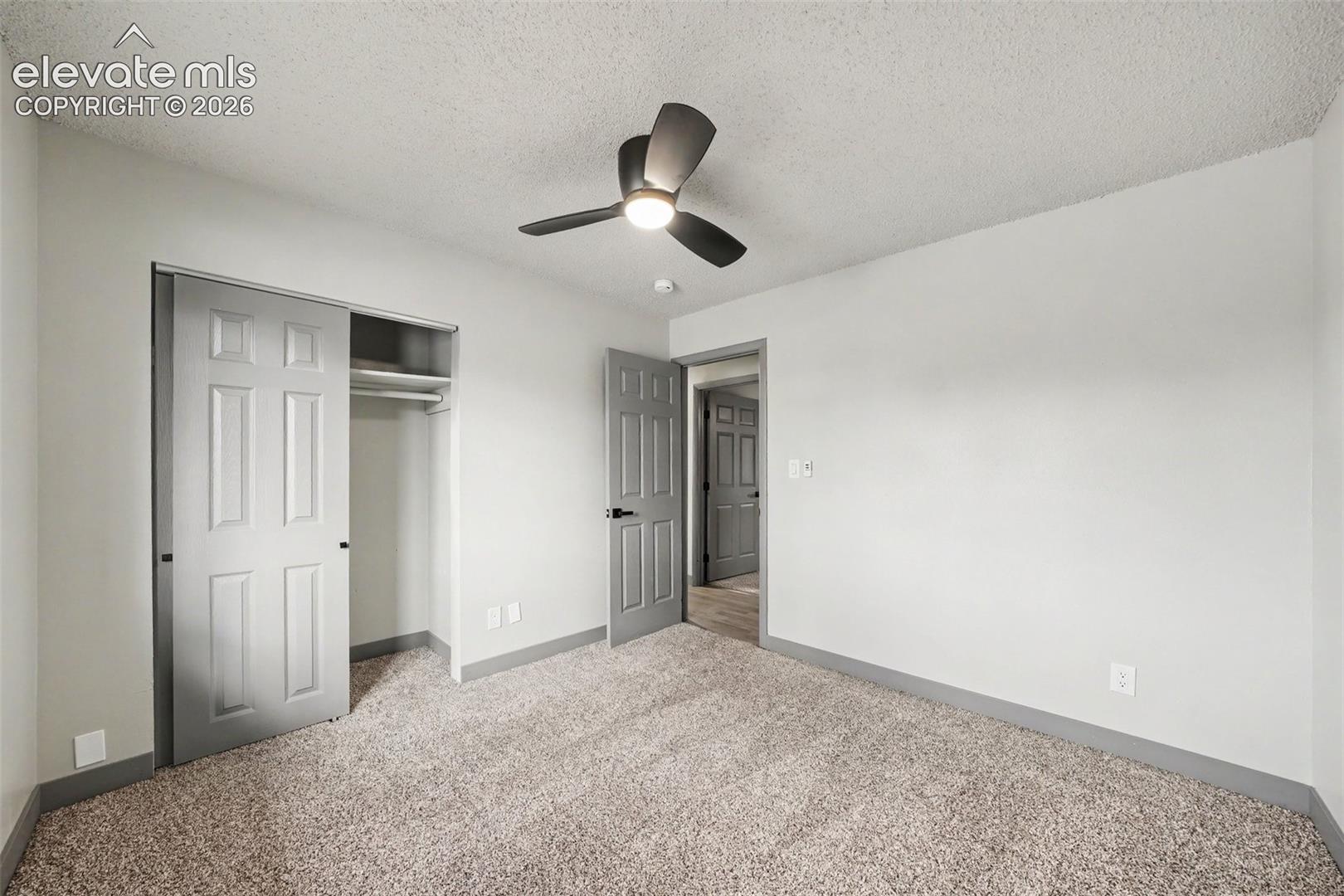 Room featuring neutral carpeting, a ceiling fan with integrated lighting, and a closet with a sliding door and built-in shelving