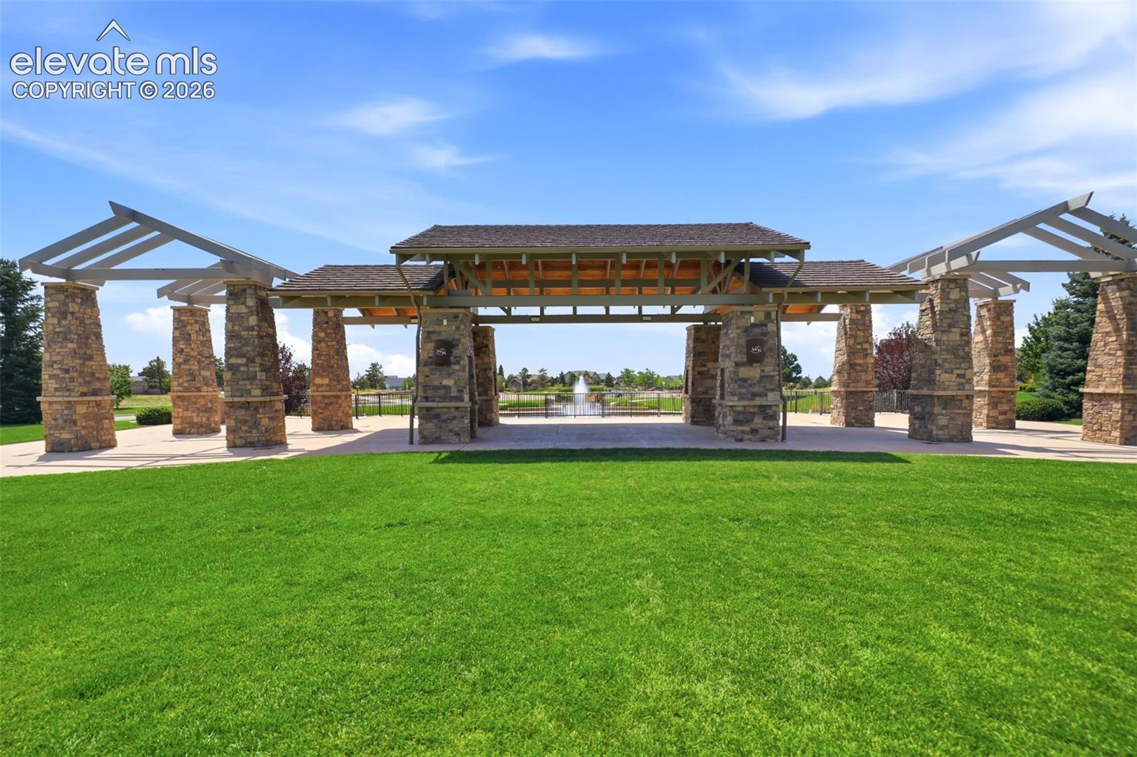 Expansive green space featuring a stone and wood beam pergola, leading to a water feature