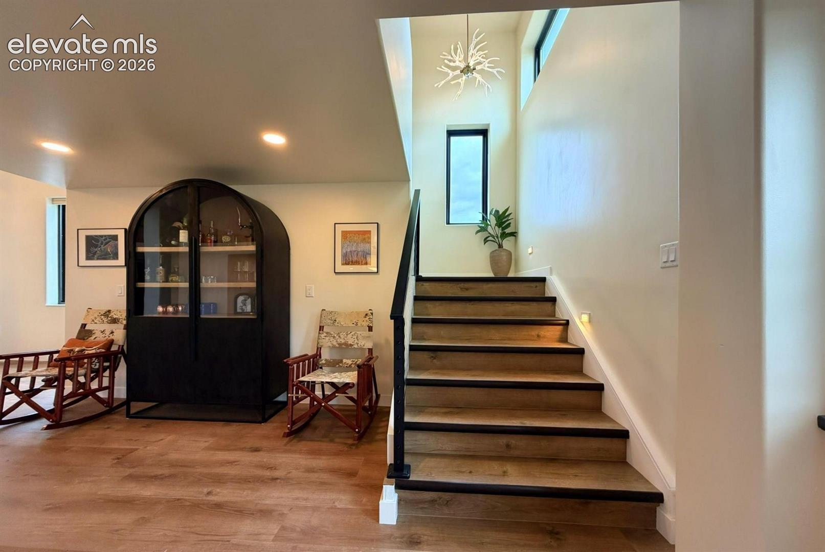 Staircase featuring wood-finish treads, a black metal handrail, recessed lighting, vertical windows, and a decorative branch-style chandelier