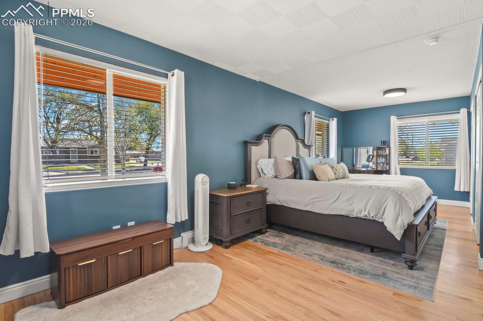 Spacious primary bedroom featuring hardwood flooring, multiple windows with blinds and a textured ceiling
