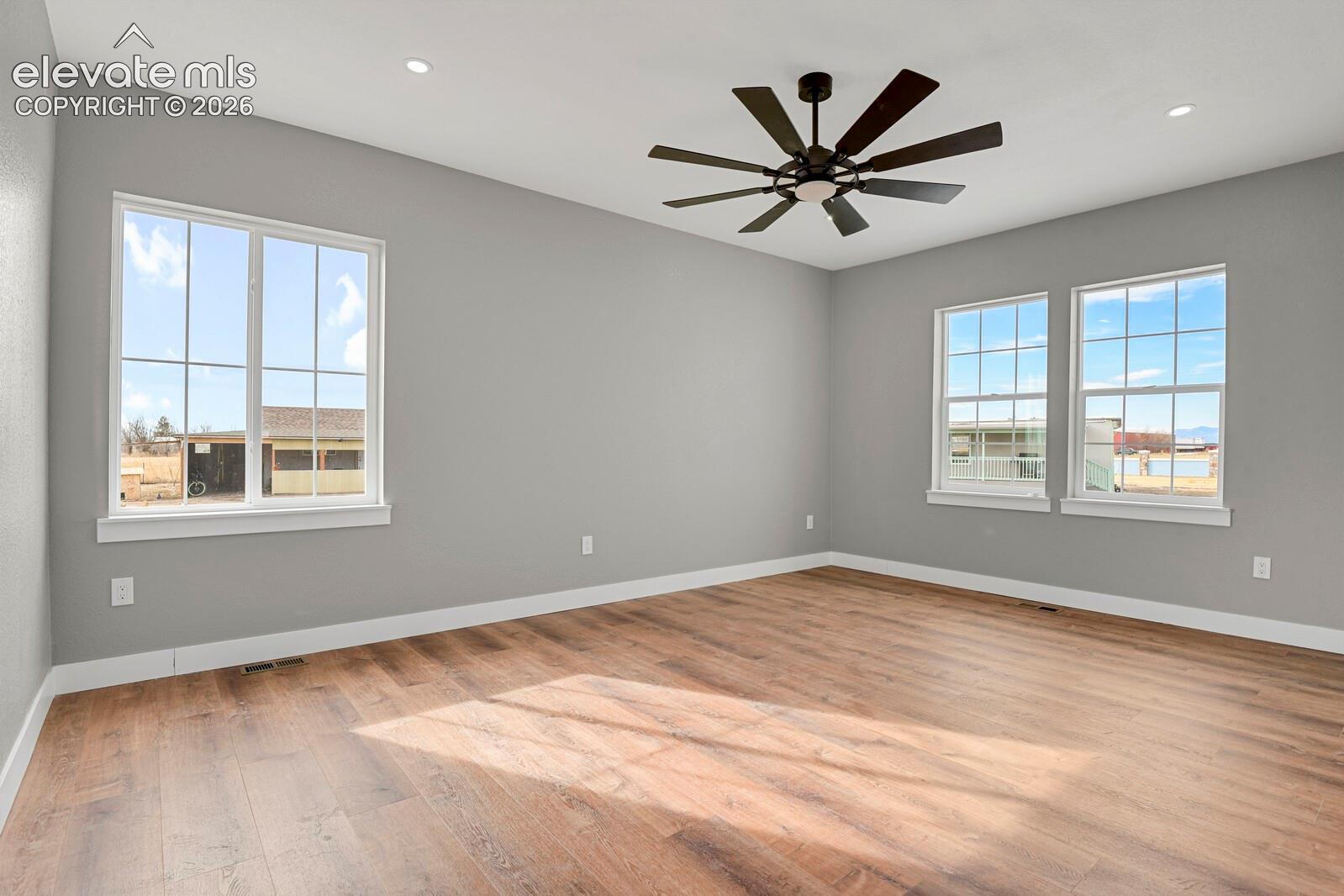 Spacious room featuring wood-finish flooring, multiple windows, a ceiling fan, and recessed lighting