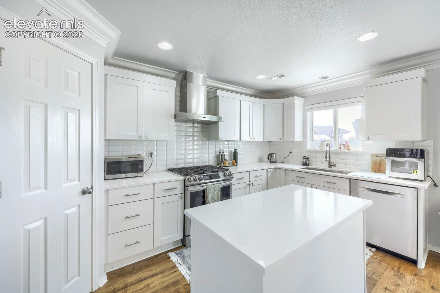 Kitchen featuring white Shaker-style cabinetry, a central island with a quartz countertop, stainless steel appliances, subway tile backsplash, and wood-finish flooring