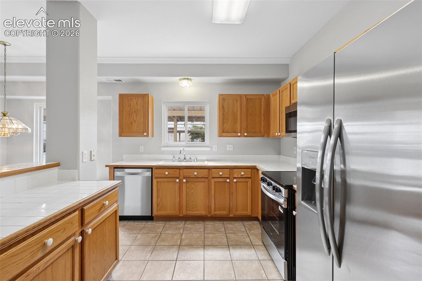 Kitchen featuring wood cabinetry, stainless steel appliances, tile flooring, and white countertops