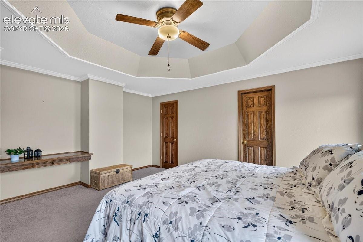 Tray ceiling featuring a central ceiling fan with integrated lighting, built-in wooden wall-mounted shelving, and solid wood-finish interior doors