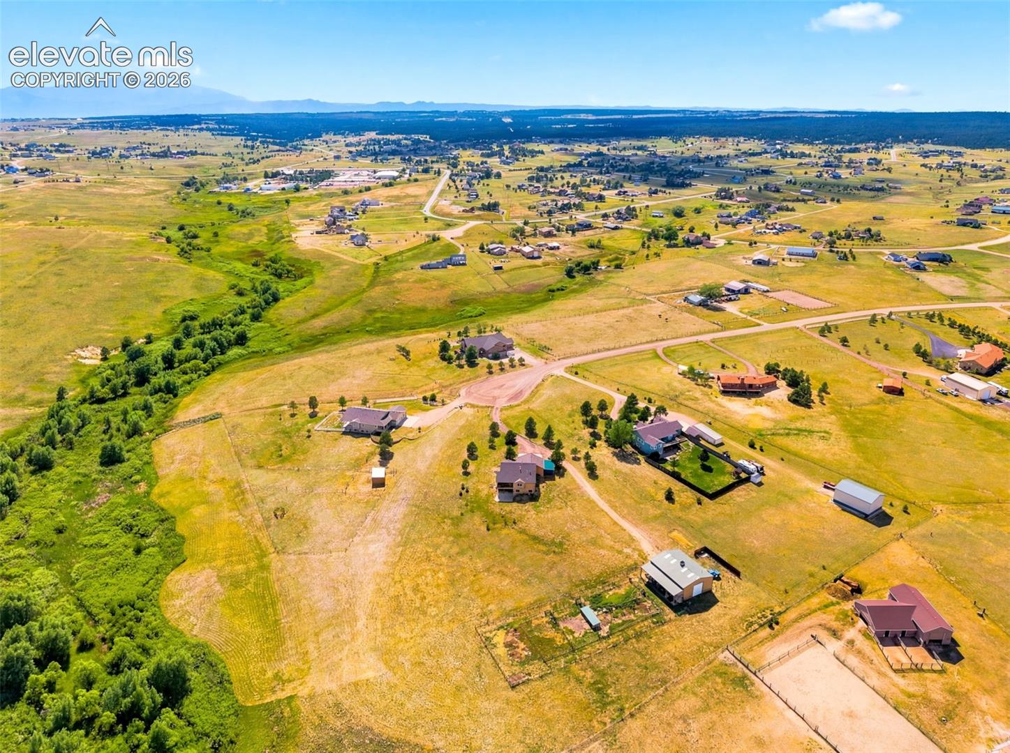 Expansive rural landscape featuring scattered residences, abundant open fields, and distant mountain ranges