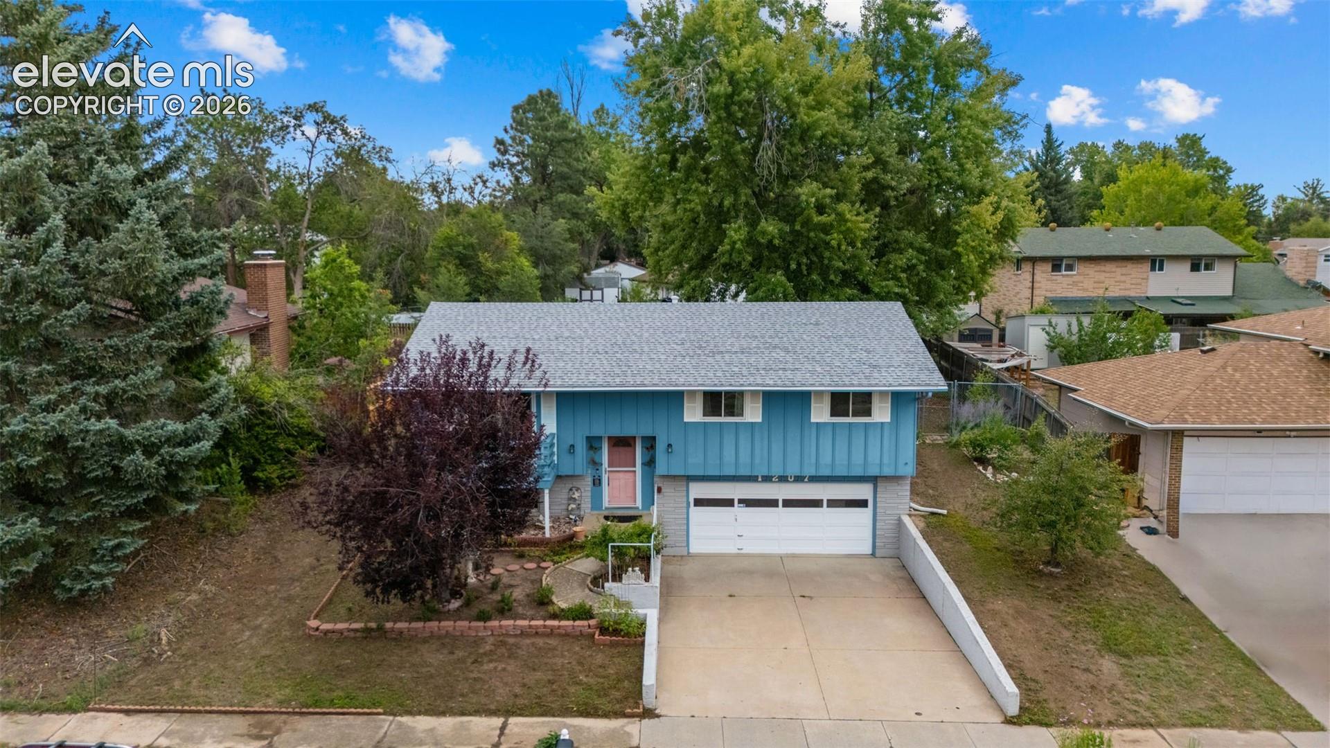 Blue exterior siding with white trim, attached two-car garage, concrete driveway, and mature landscaping