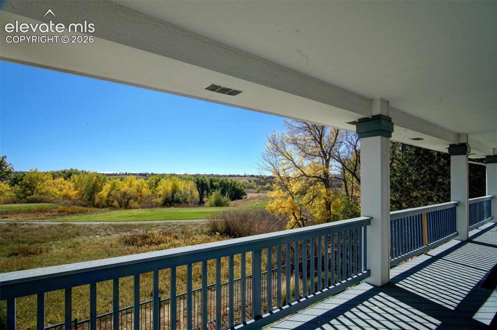 Covered exterior porch featuring painted wood railings, square structural columns, and open-air space overlooking natural terrain with mature trees