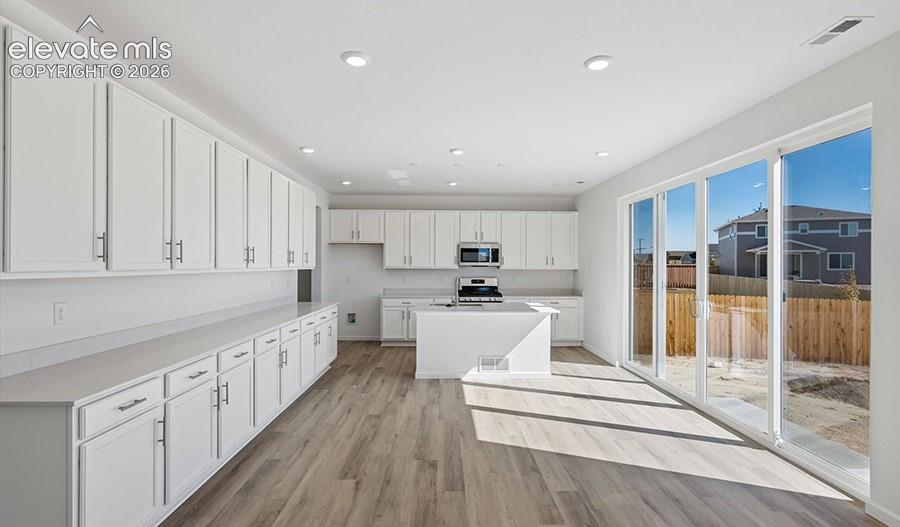 Kitchen featuring white cabinetry, a center island, wood-finish flooring, recessed lighting, and large sliding glass doors