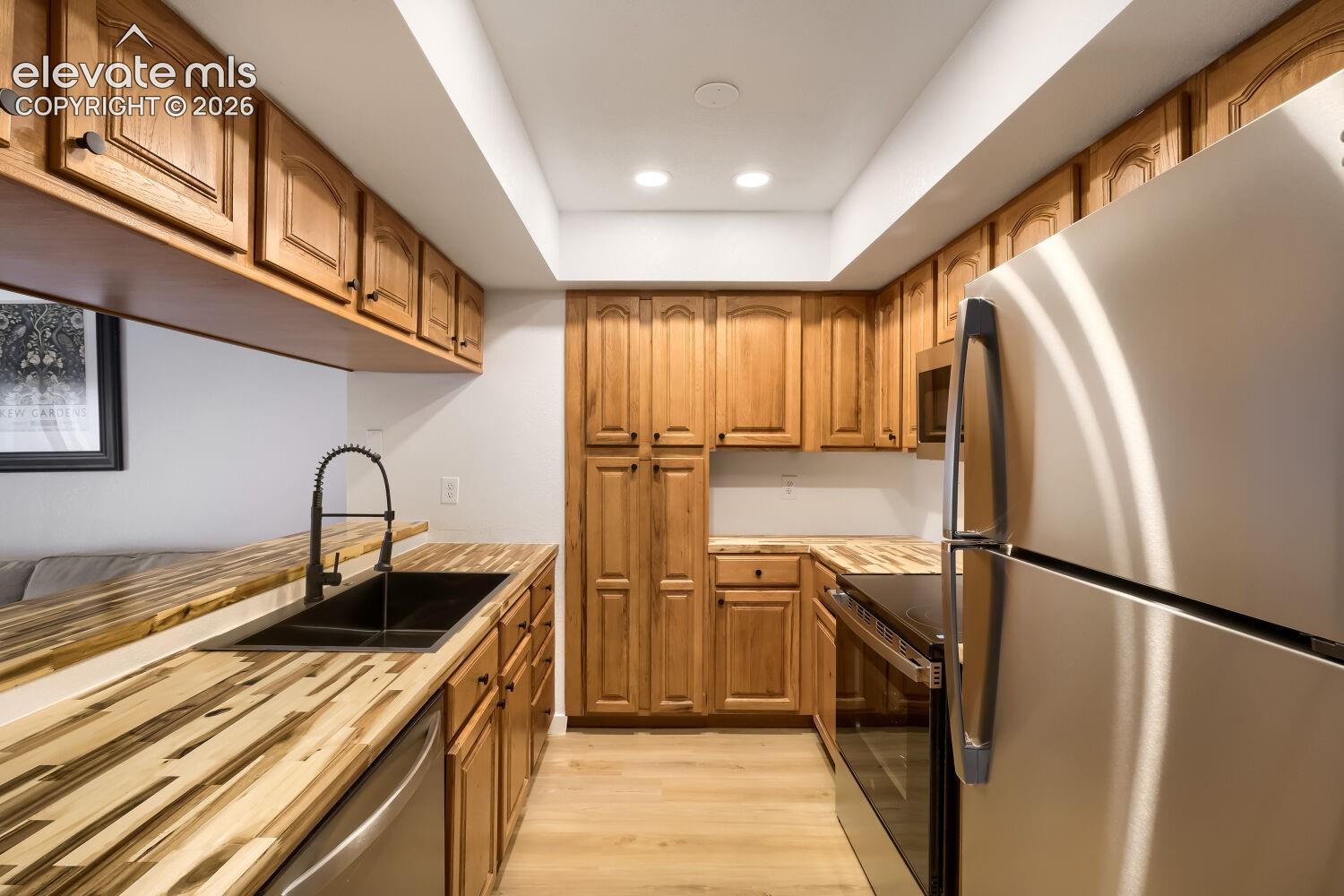 Kitchen featuring wood cabinetry, butcher block countertops, stainless steel appliances, a matte black kitchen faucet, and a dual-basin drop-in sink