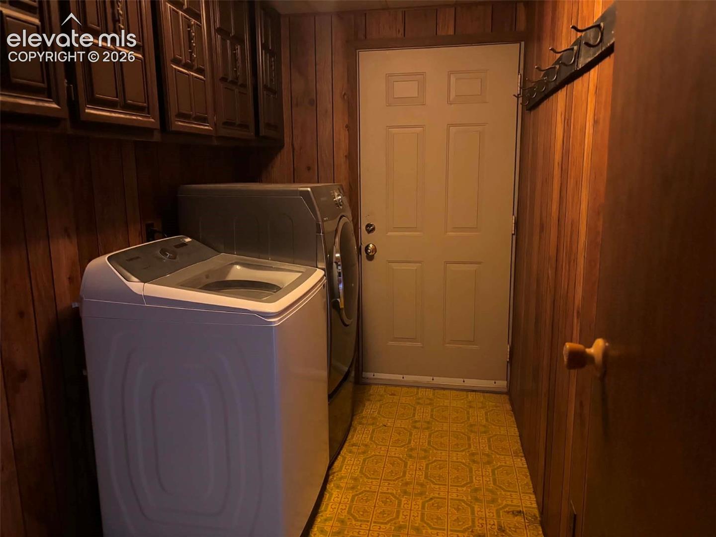 Laundry area featuring wood-paneled walls, built-in upper cabinetry, patterned flooring, and a wall-mounted garment rack