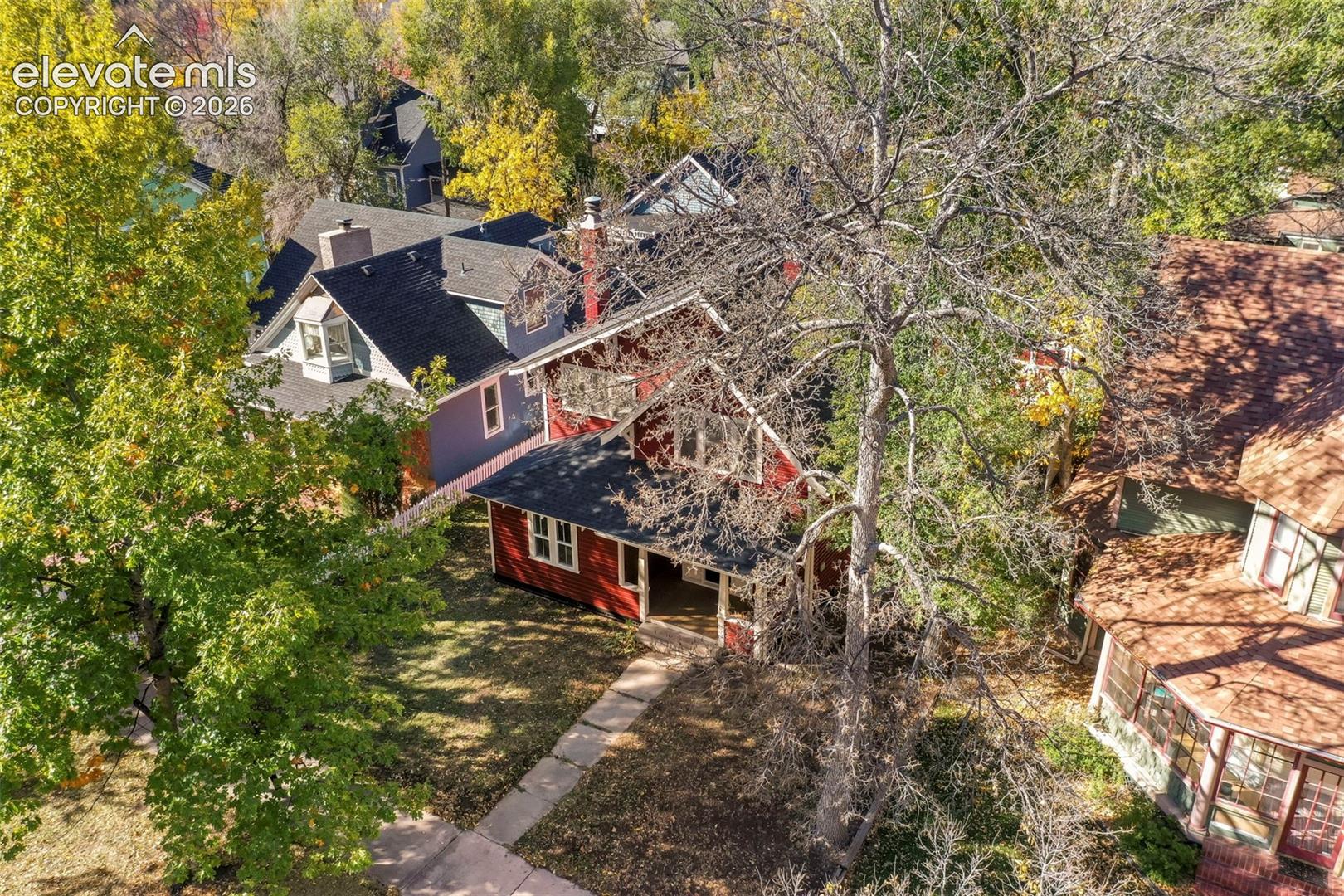 Two-story residence featuring a red exterior, dark asphalt shingle roofing, front porch, stone walkway, and mature trees