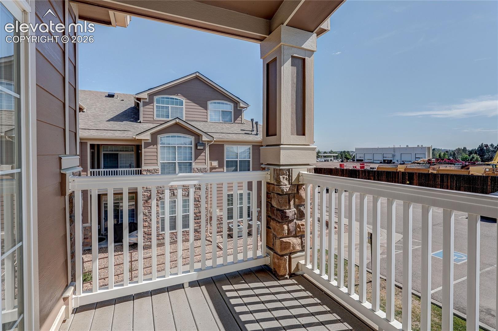 Covered balcony featuring composite decking, white railing, and a stone-clad support column