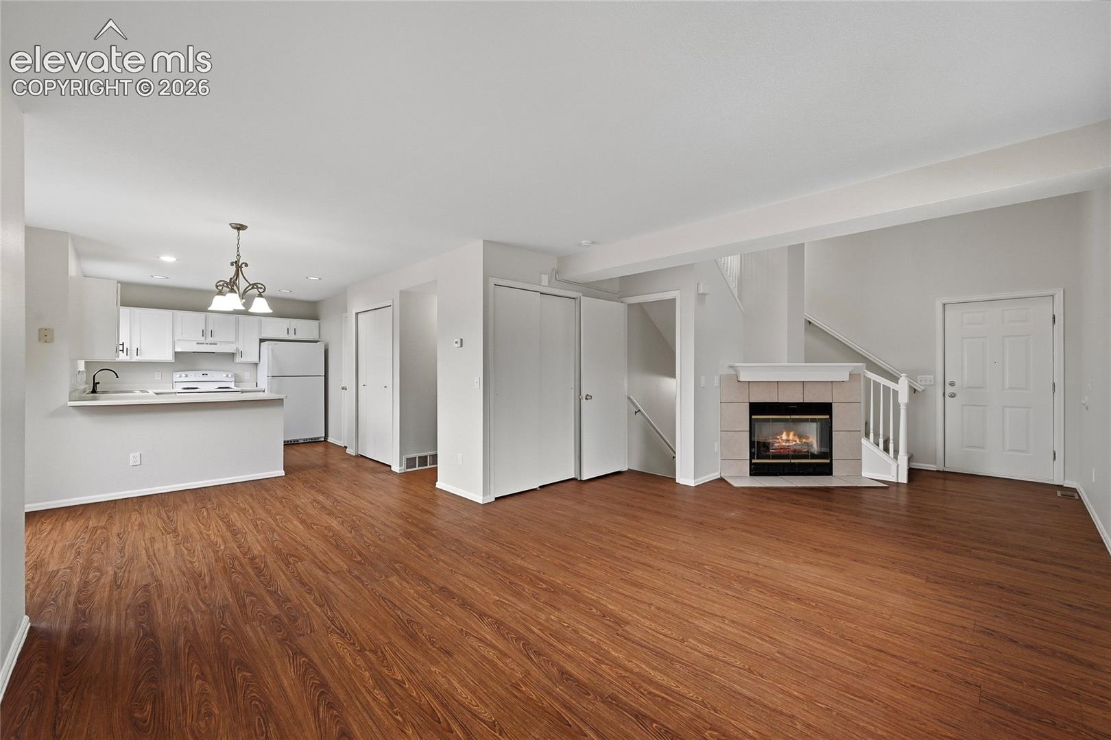 Open-concept interior featuring wood-finish flooring, a fireplace with a ceramic tile surround, white cabinetry, and a multi-pendant light fixture