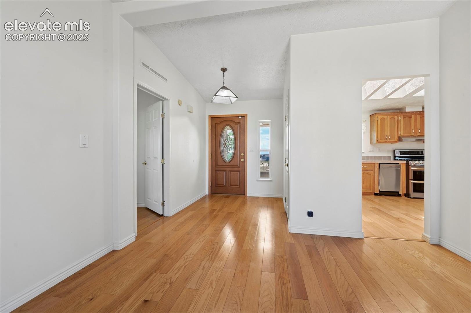 Hardwood flooring throughout, vaulted ceiling, and an arched entry door with decorative glass
