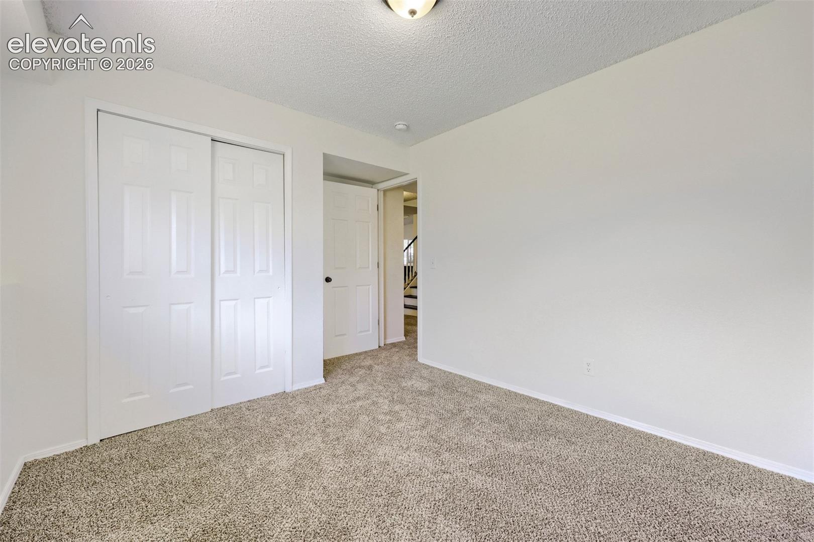 Carpeted flooring, white walls, built-in closet with sliding panel doors, and overhead lighting