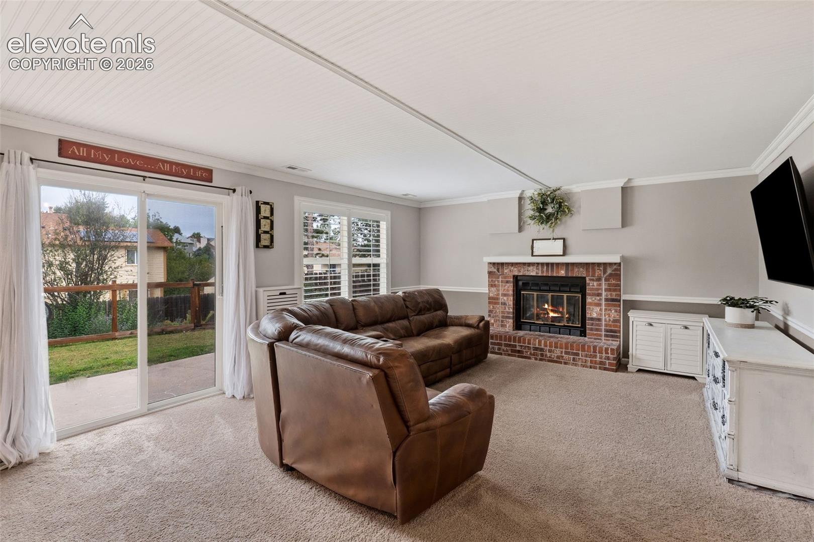 Spacious family room featuring a brick fireplace with mantel, wall-mounted television, carpet flooring, and French door access to the backyard