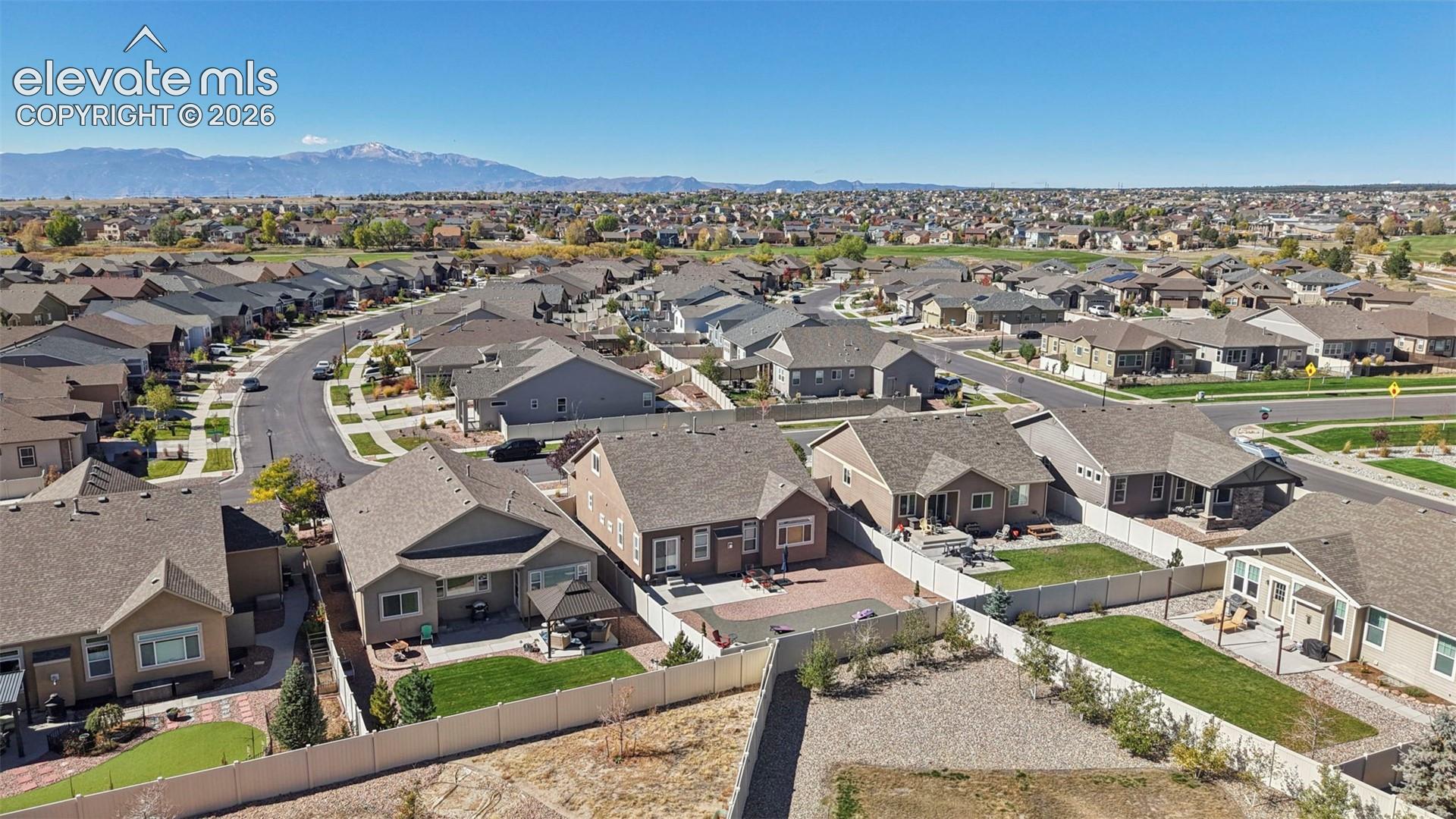 Aerial perspective of residential neighborhood featuring fenced backyards, paved patios, manicured lawns, and prominent mountain backdrop