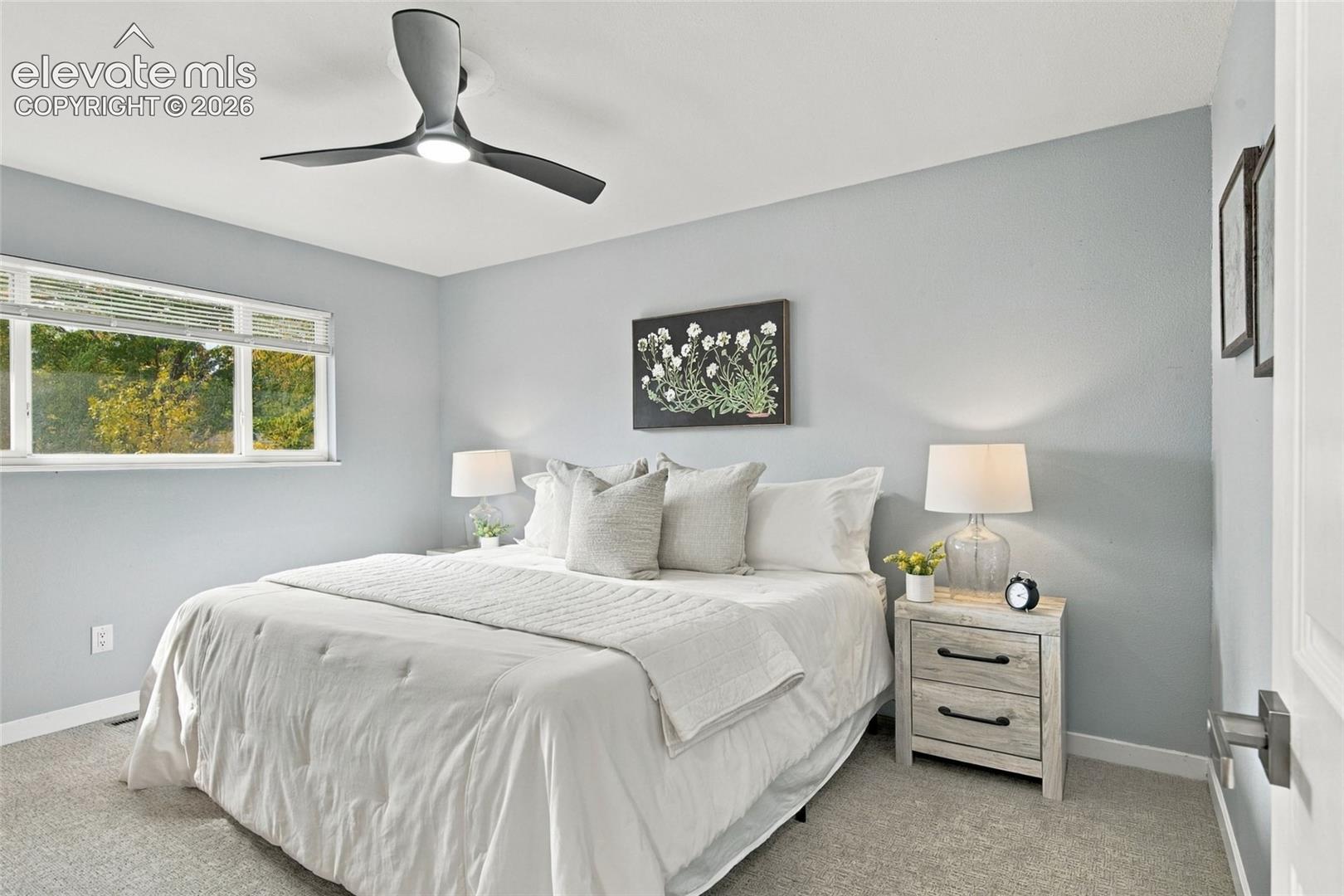 Neutral-toned interior space featuring three-blade modern ceiling fan with integrated lighting, expansive window with horizontal blinds, and neutral carpeting