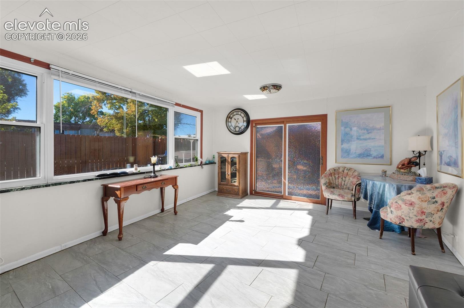 Sunroom featuring large windows, stone-tile flooring, dual skylights, and sliding glass patio doors
