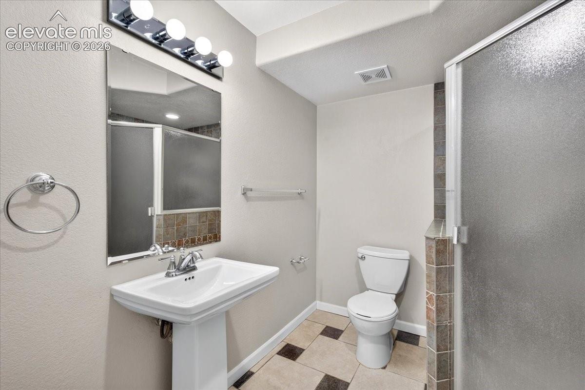 Pedestal sink with chrome faucet, vanity lighting, tile flooring, and frosted glass shower enclosure