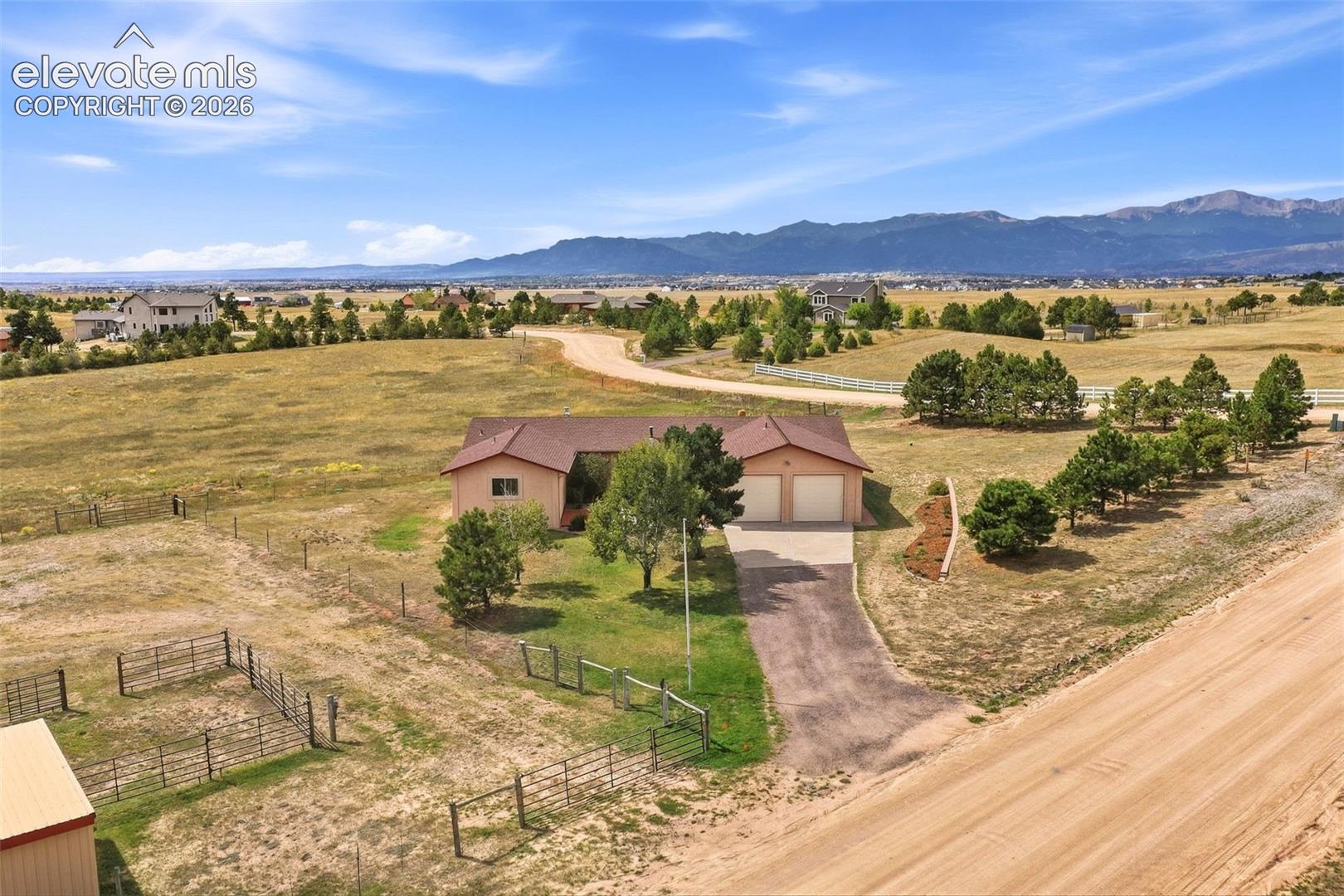 Spacious rural property featuring a single-story residence, attached two-car garage, expansive outdoor areas with fencing, and a gravel driveway
