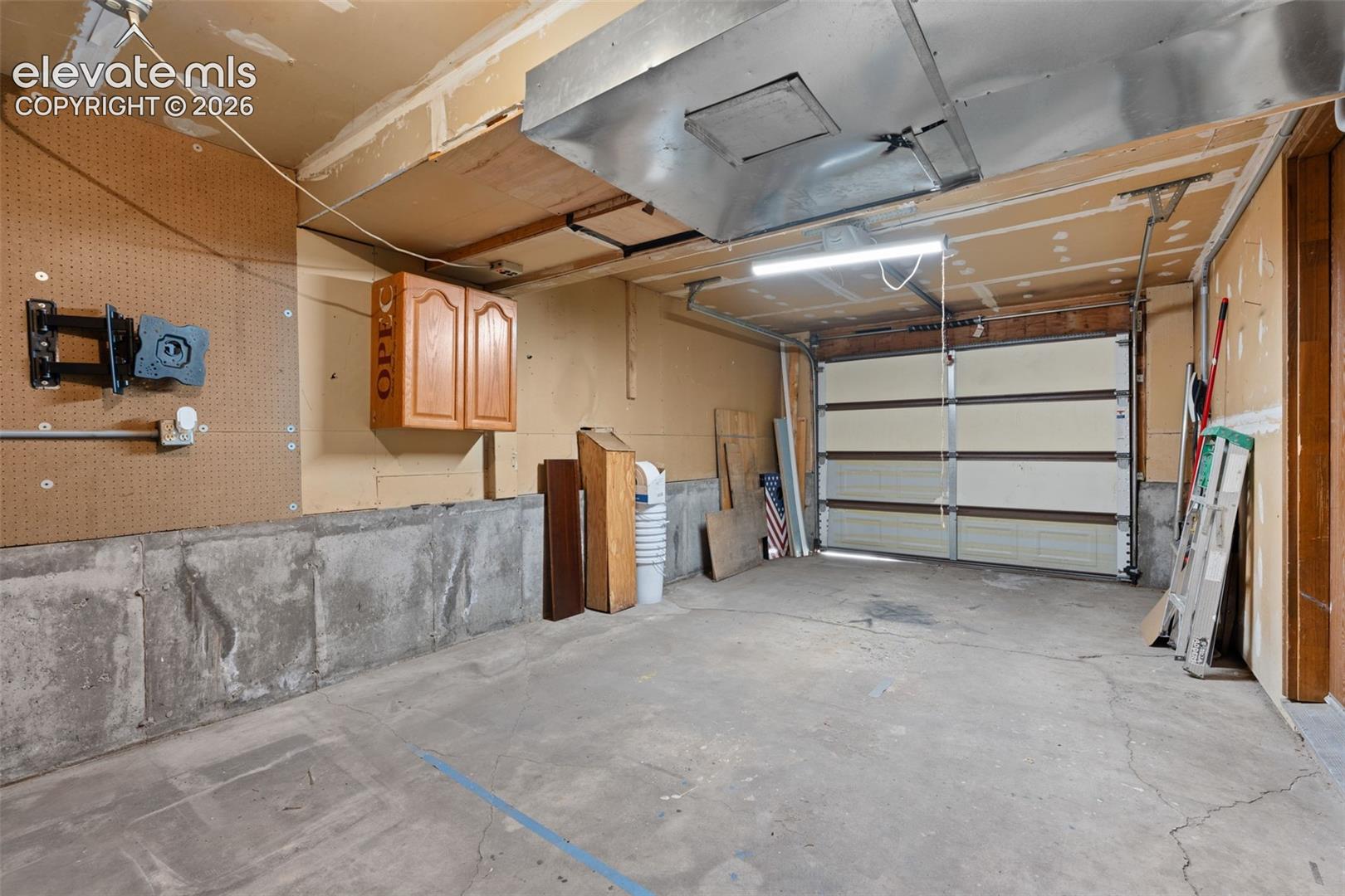 Attached garage featuring concrete flooring, an overhead garage door, built-in cabinetry, and exposed ductwork