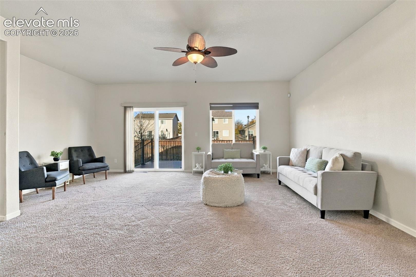 Neutral-toned living space featuring wall-to-wall carpeting, a multi-blade ceiling fan with integrated lighting, and glass sliding doors providing exterior access