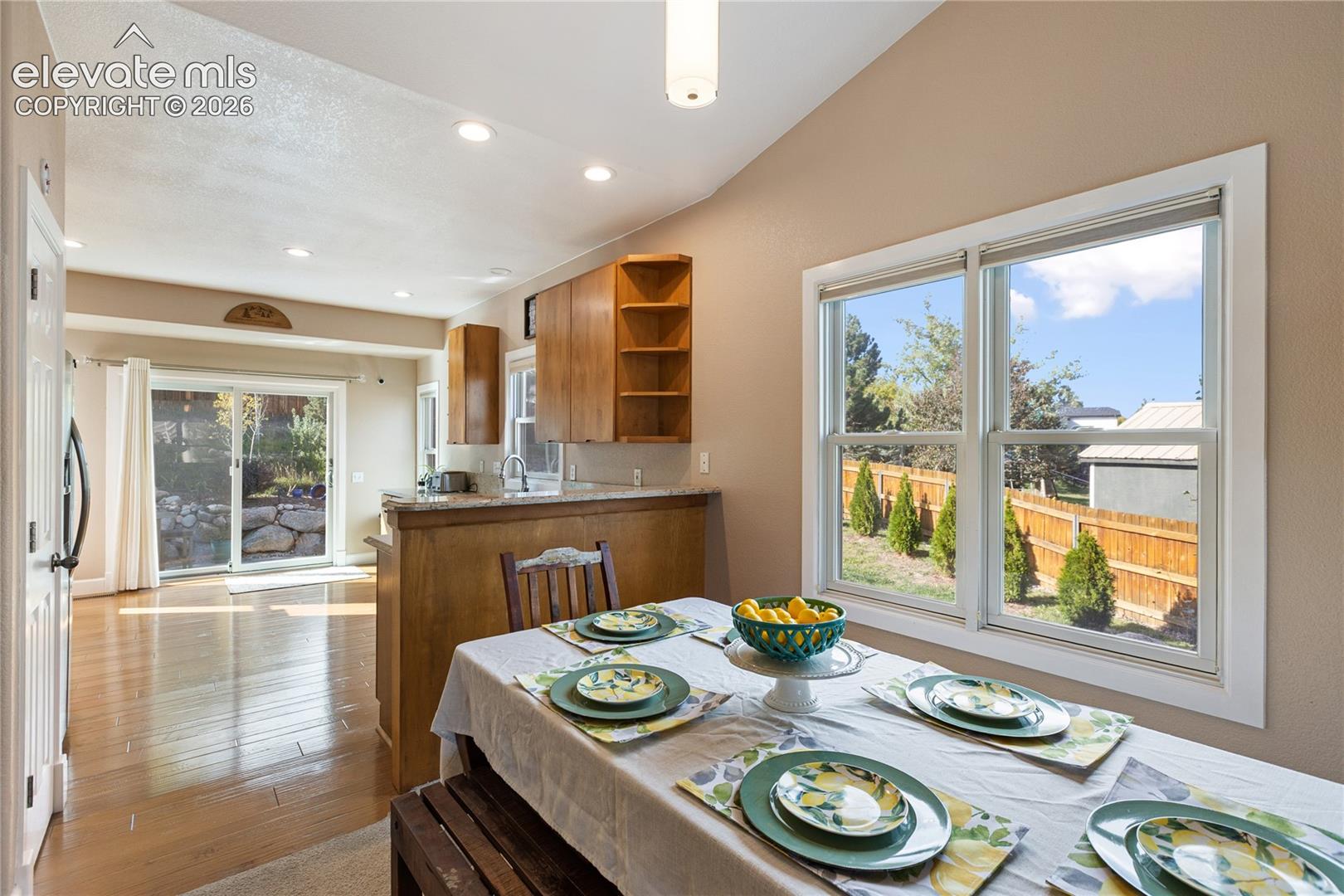 Vaulted ceiling with recessed lighting, wood-finish flooring, sliding glass door, double-hung windows, and wood cabinetry